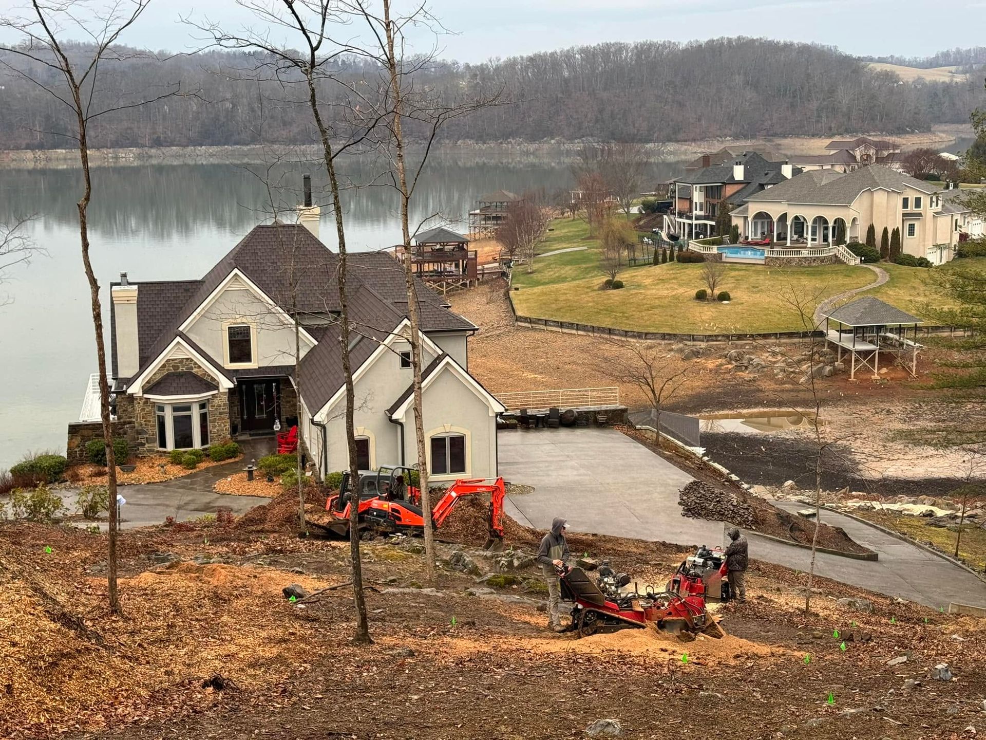 Lakefront home with damaged landscaping, fallen debris, and a muddy driveway after flooding or erosion