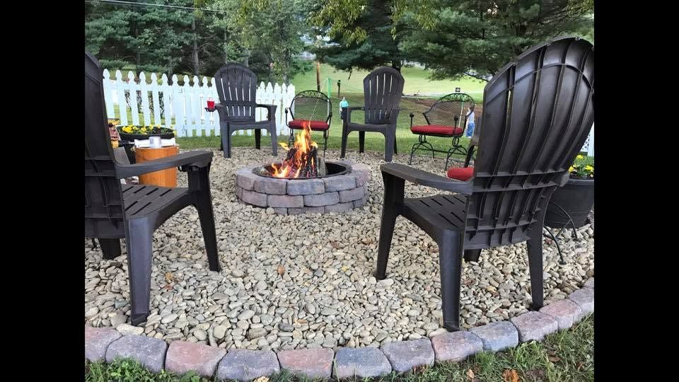 Circular stone fire pit surrounded by black chairs on a gravel patio in a backyard garden