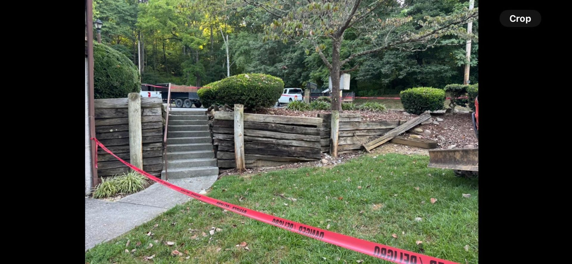 Cordoned-off garden path and stone retaining wall with red caution tape in a park-like area