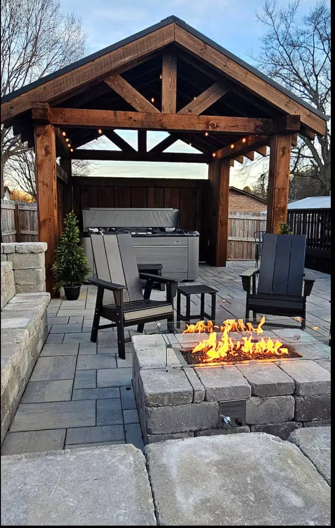 Stone patio fire pit seating under a wooden pergola in an outdoor backyard.