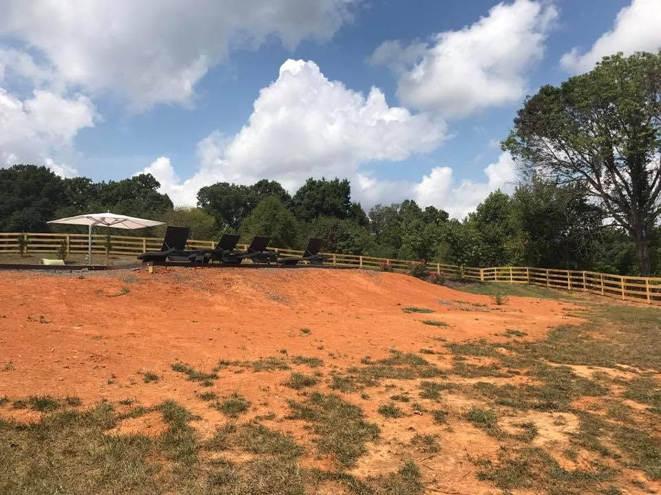 Reddish dirt paddock with wooden fencing, trees, and a partly cloudy sky