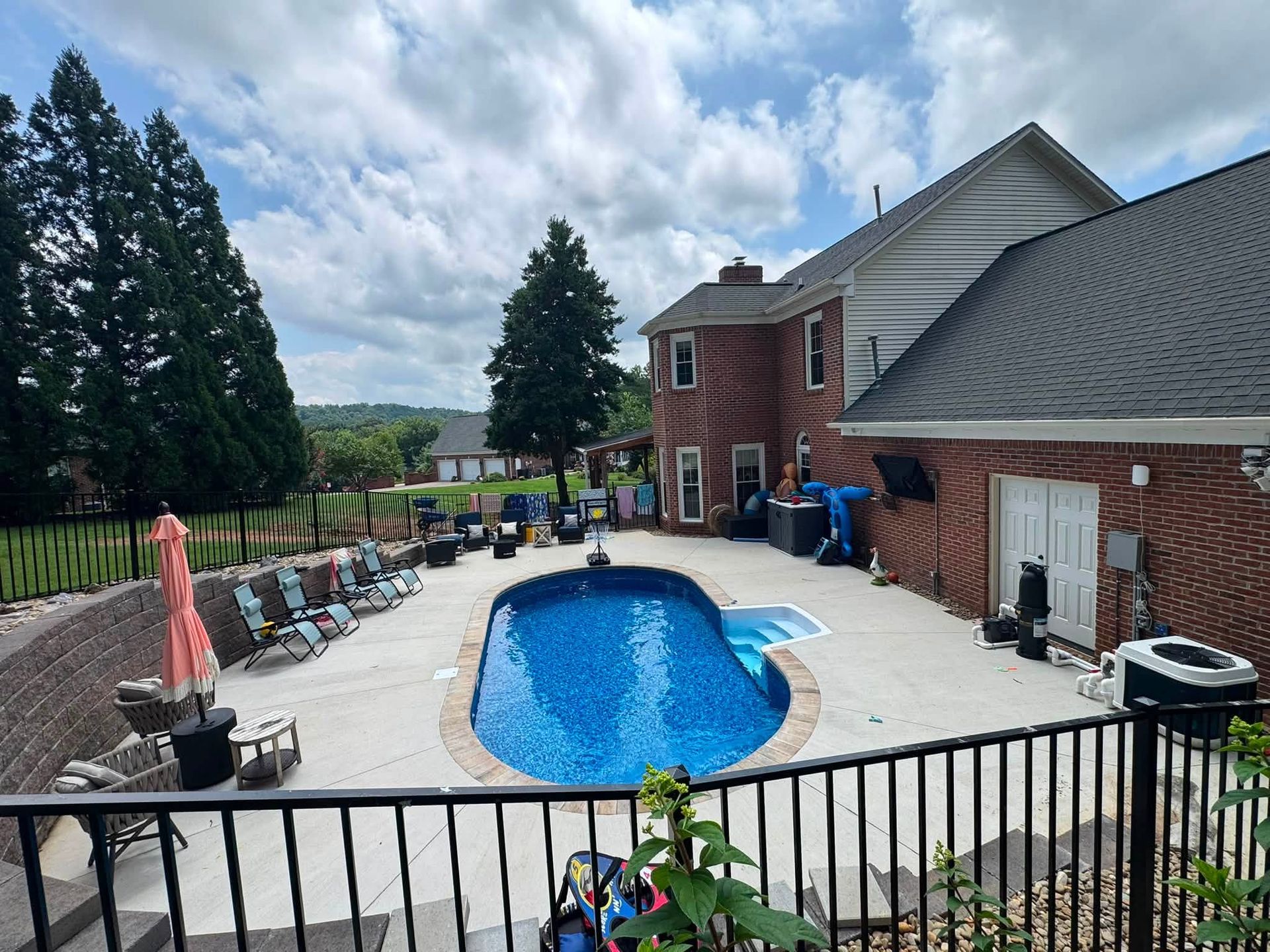 Backyard patio with a small blue pool beside a brick house and lounge chairs under tall trees