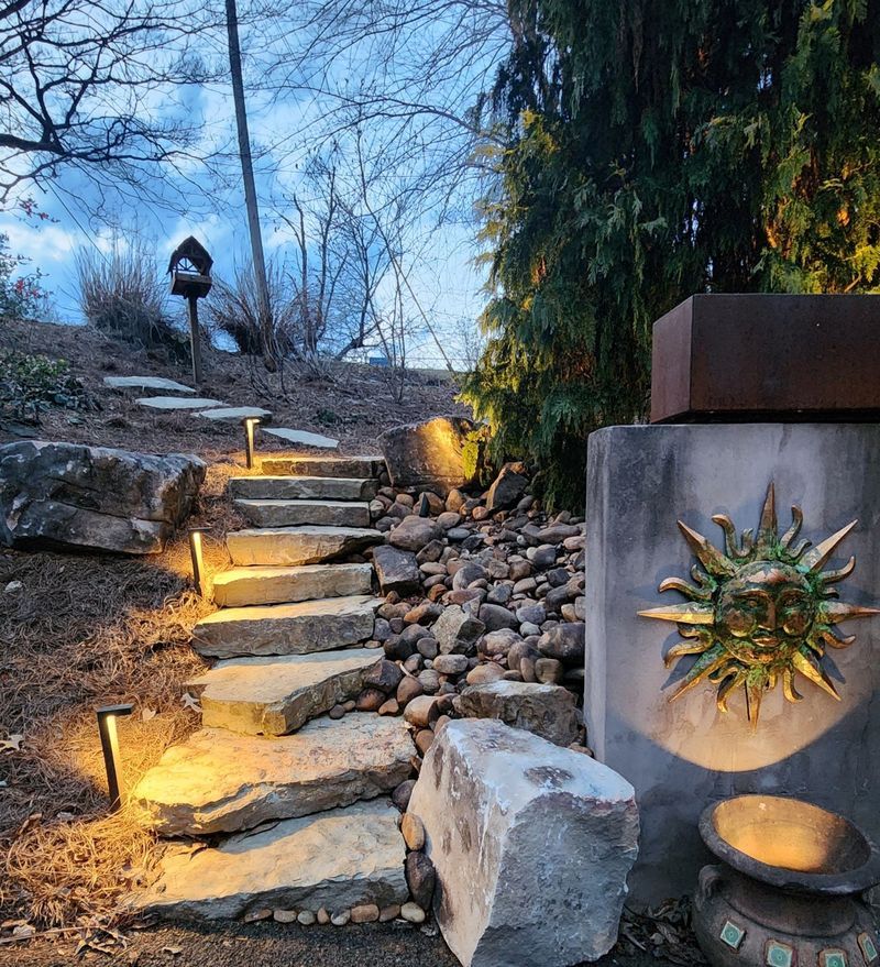 Lit stone steps in a garden path at dusk, with warm path lights and a wall-mounted succulent planter.