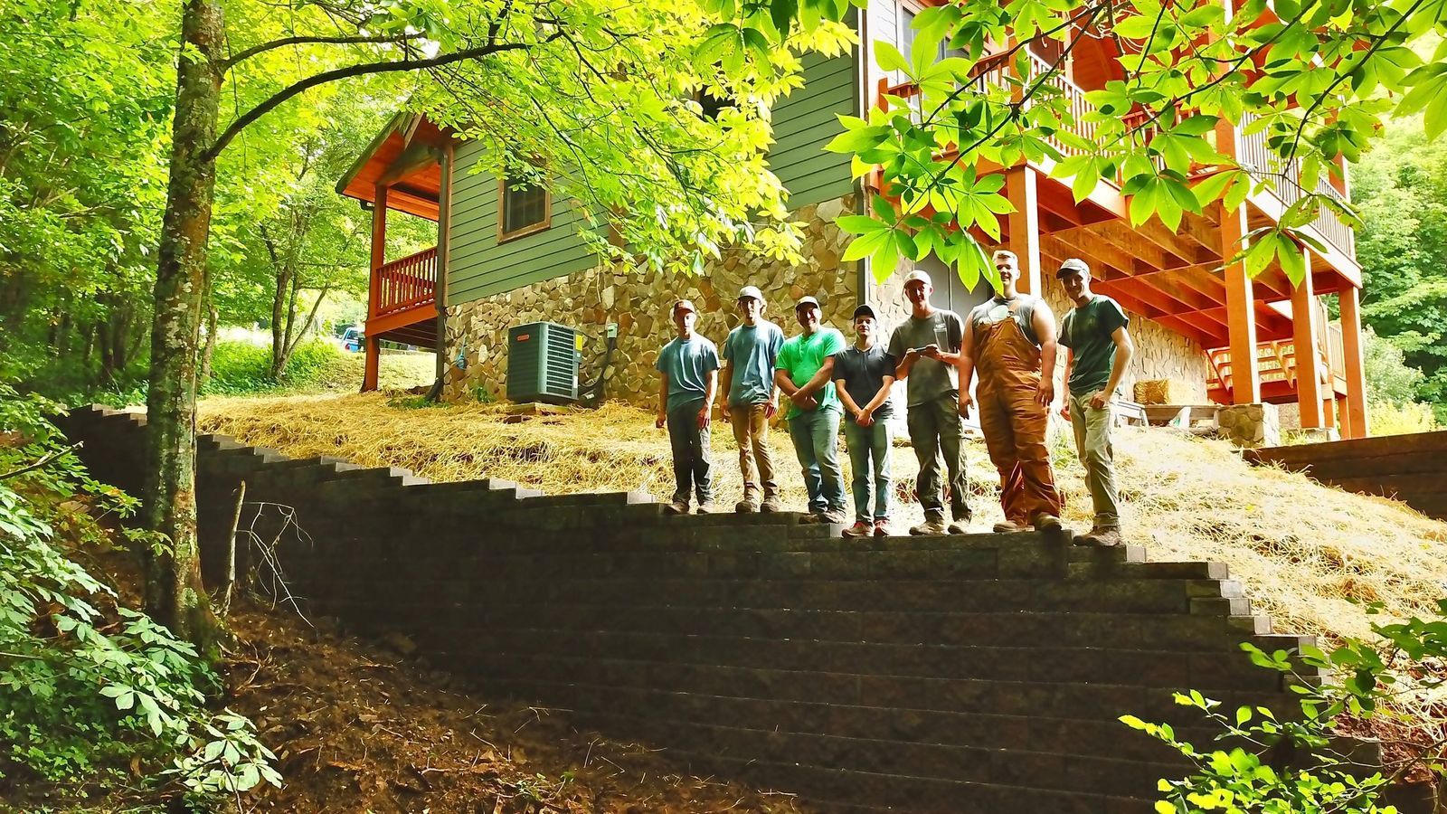 Hikers standing on stone steps by a red lodge in a leafy forest hillside