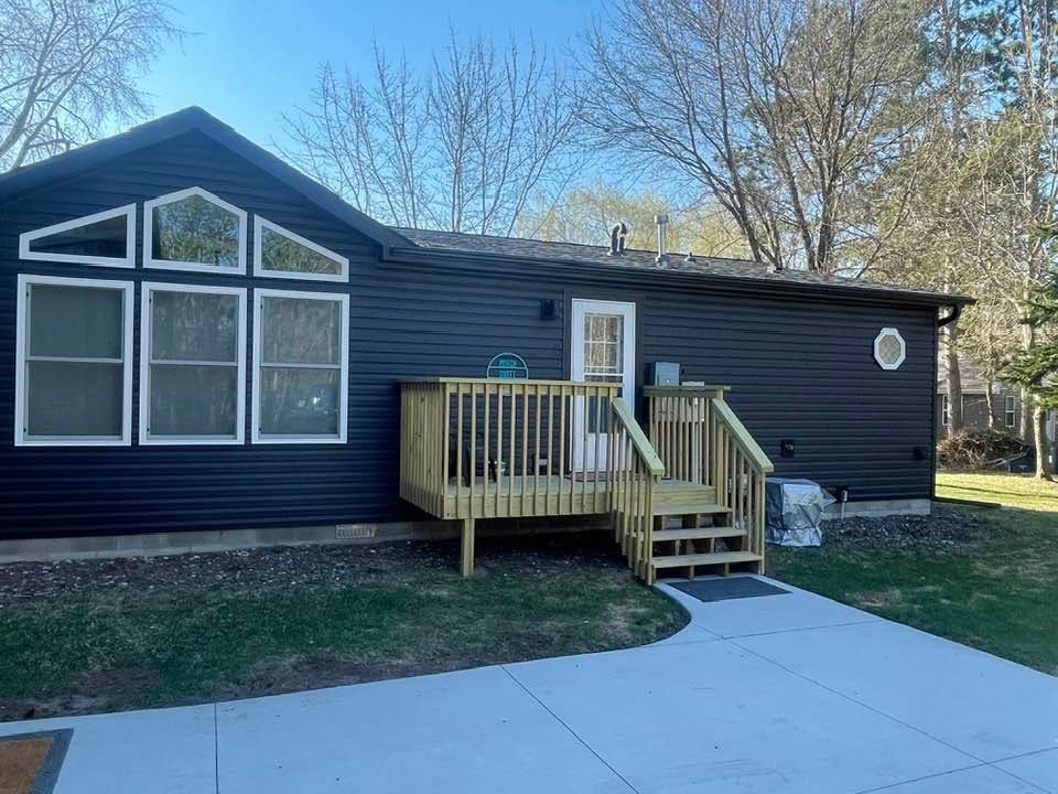 Dark blue house with a small wooden porch and steps beside a concrete driveway.