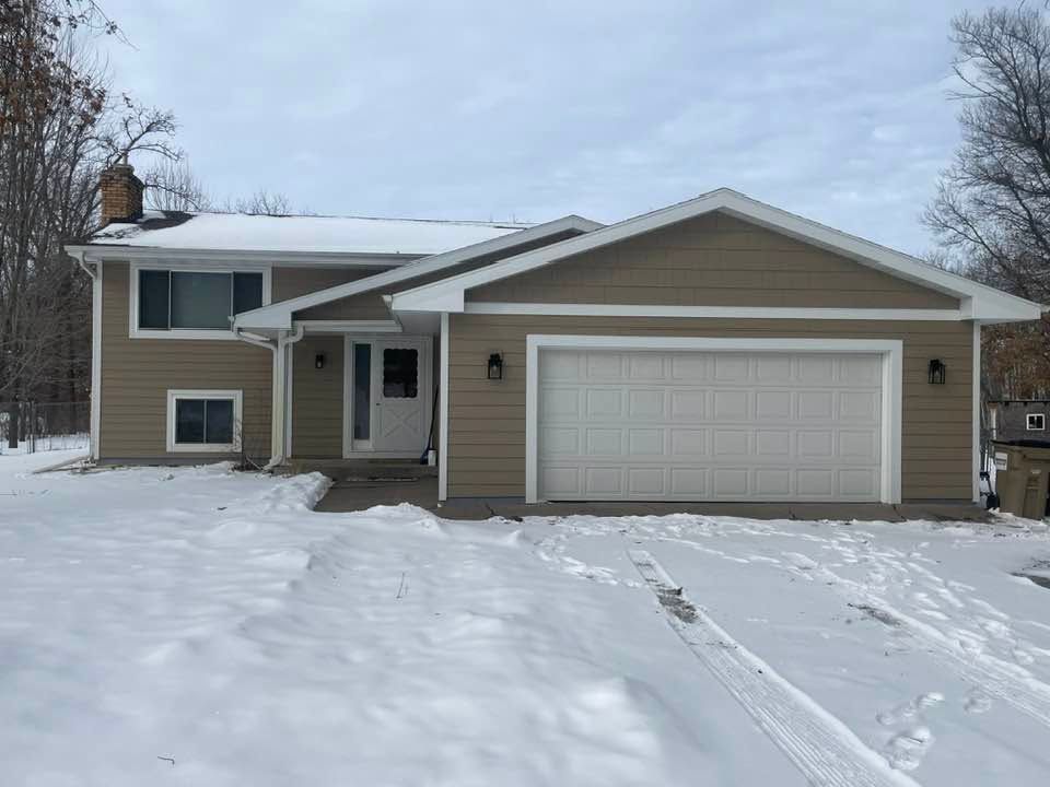 Snow-covered suburban house with a two-car garage and front porch in winter.
