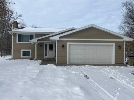 Snow-covered suburban house with a two-car garage and front porch in winter.