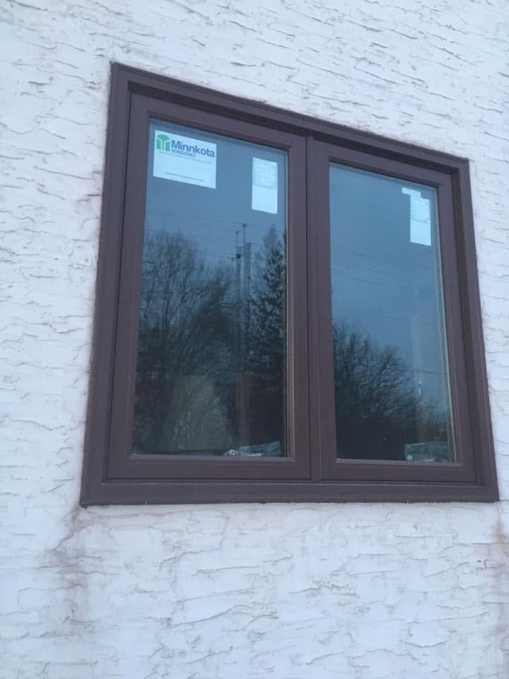 Brown-framed double window set in a white stucco wall, with tree reflections in the glass.