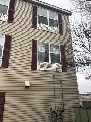 Exterior of beige apartment building with maroon shutters and utility meters near the wall