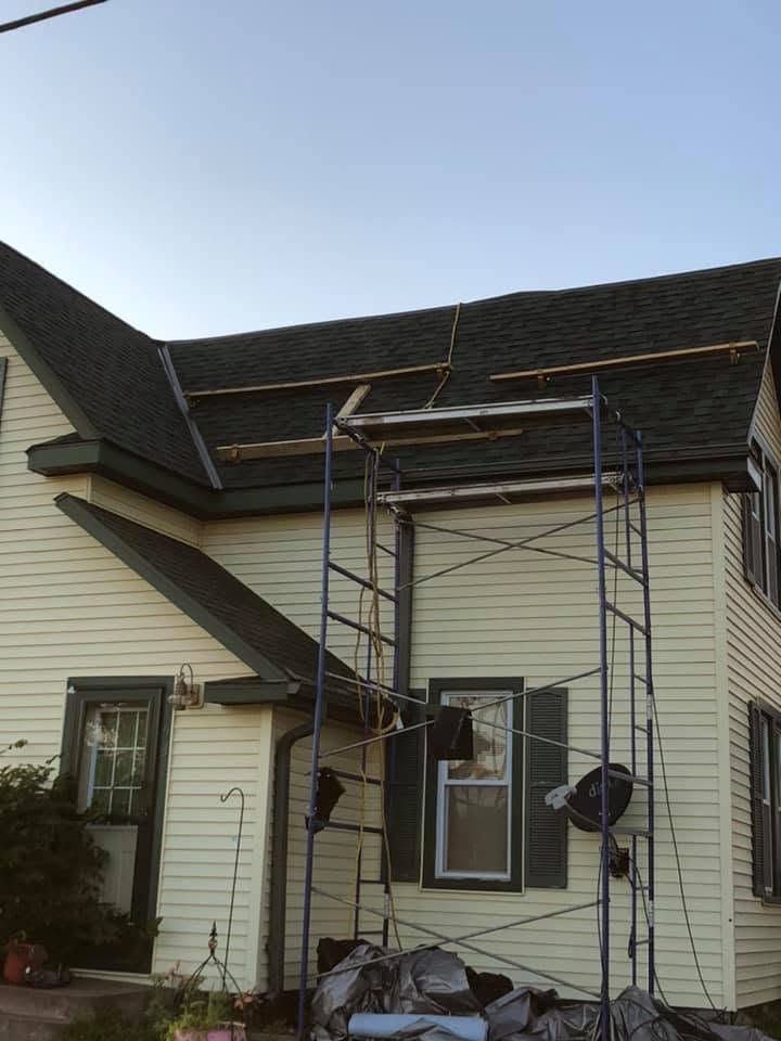 Scaffold against a beige house with dark roof and two workers near the front door.