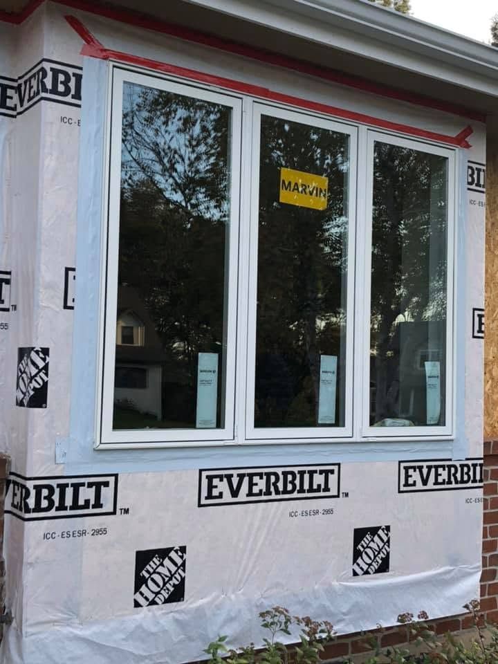 Window framed in house wrap with EverBilt branding and a yellow sticker in the center window