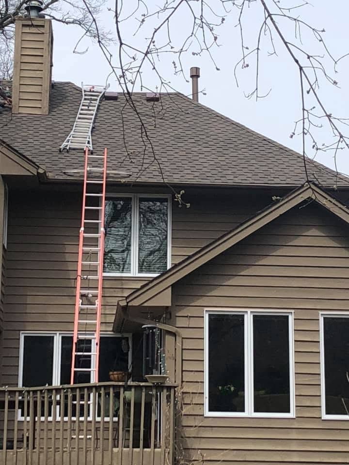 Two ladders on a brown house roof beside the chimney, with a long ladder spanning the roof