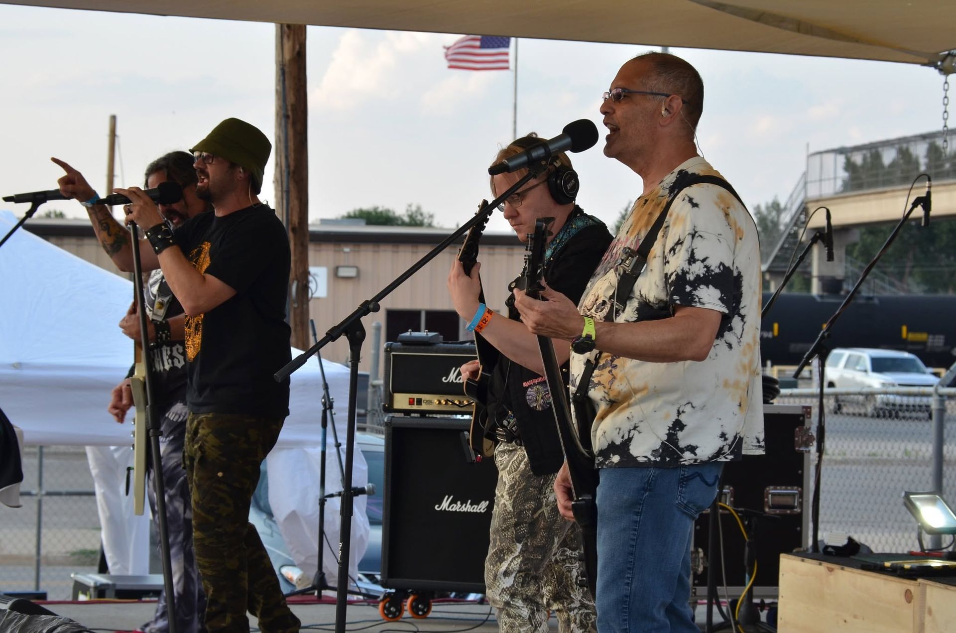 Live band performing outdoors on stage with microphones, guitars, and amplifiers.