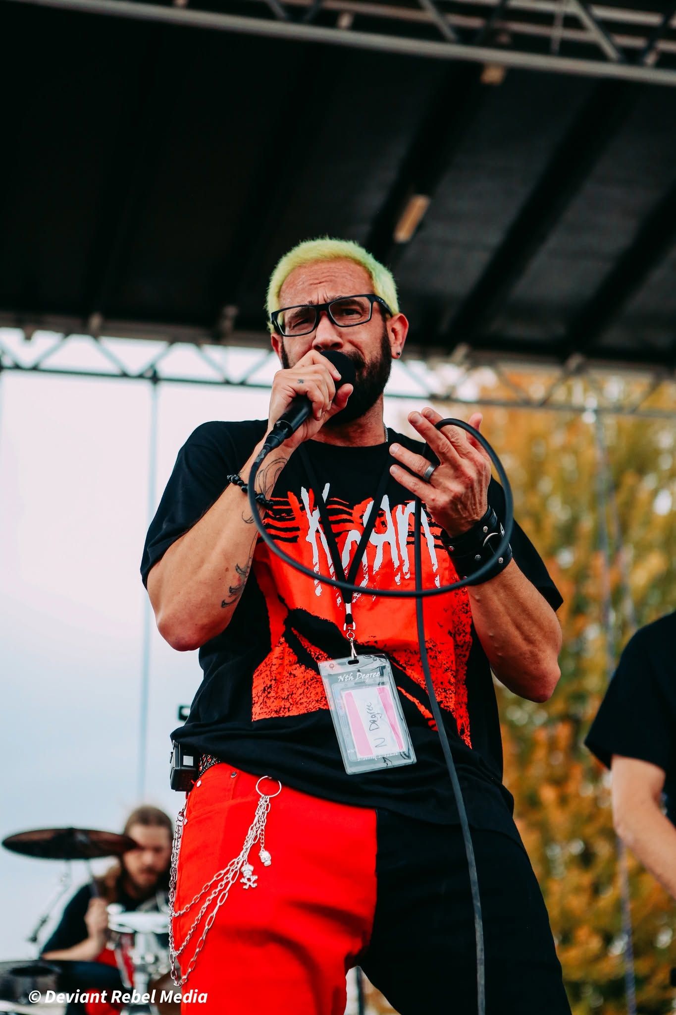 Singer on stage wearing a black-and-red shirt and red pants, holding a microphone during a live performance