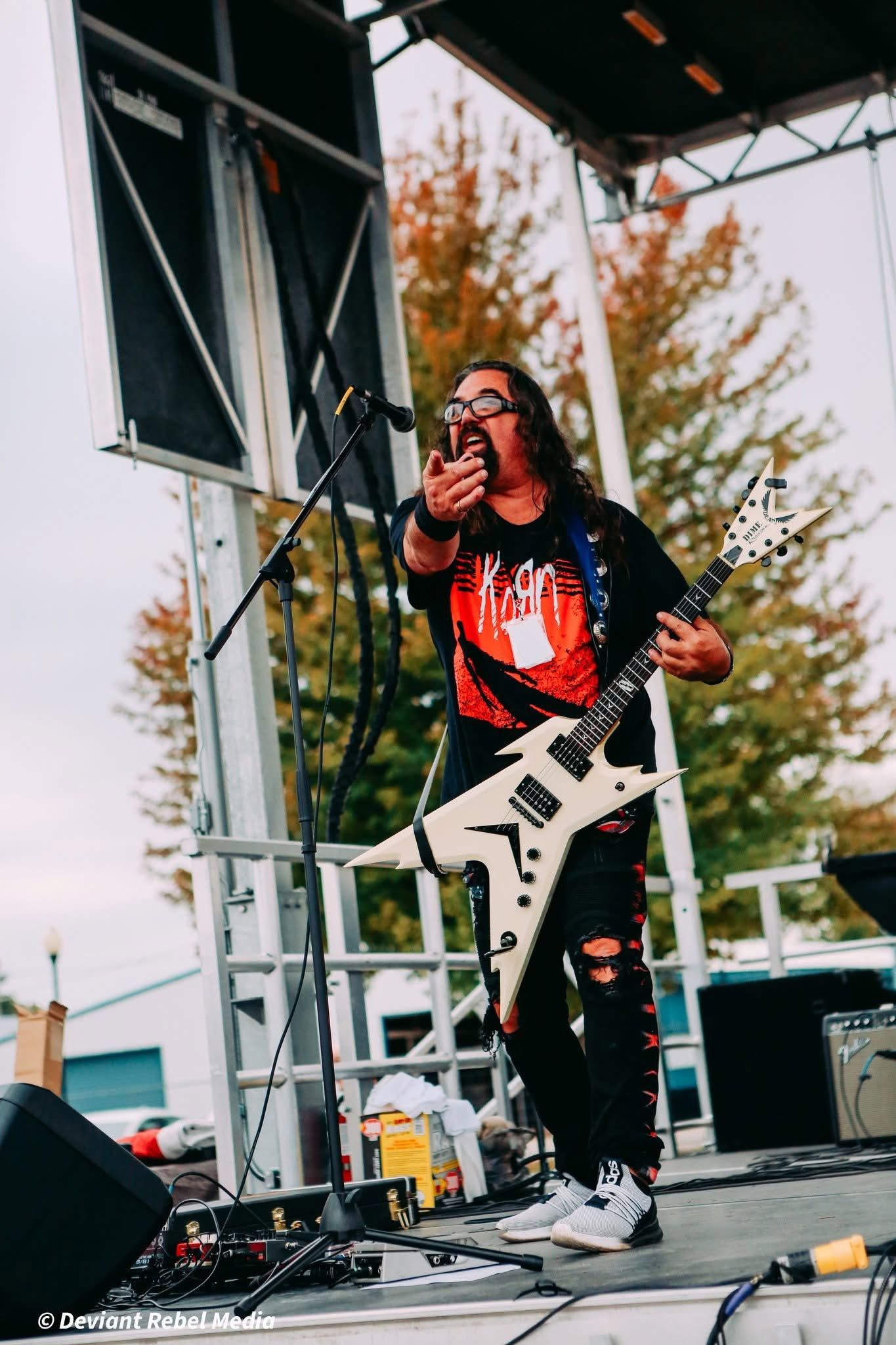 Singer-guitarist performing on an outdoor stage with a microphone and white electric guitar