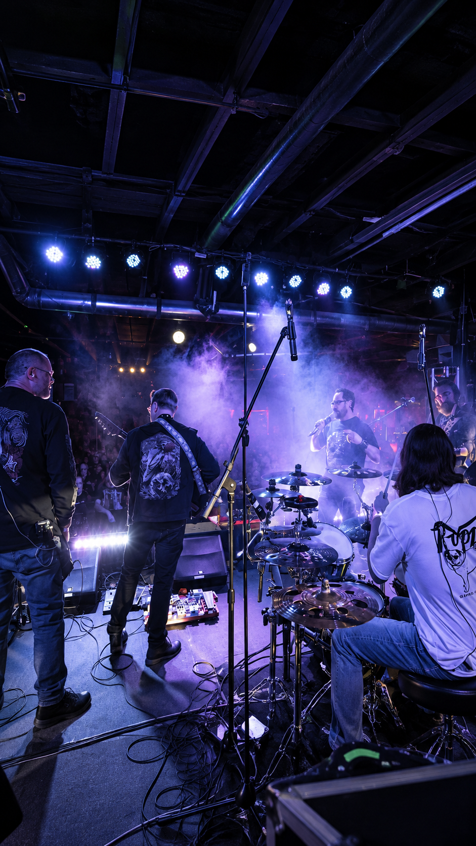 Live band performing on a smoky stage under purple-blue lights, with musicians and instruments visible.