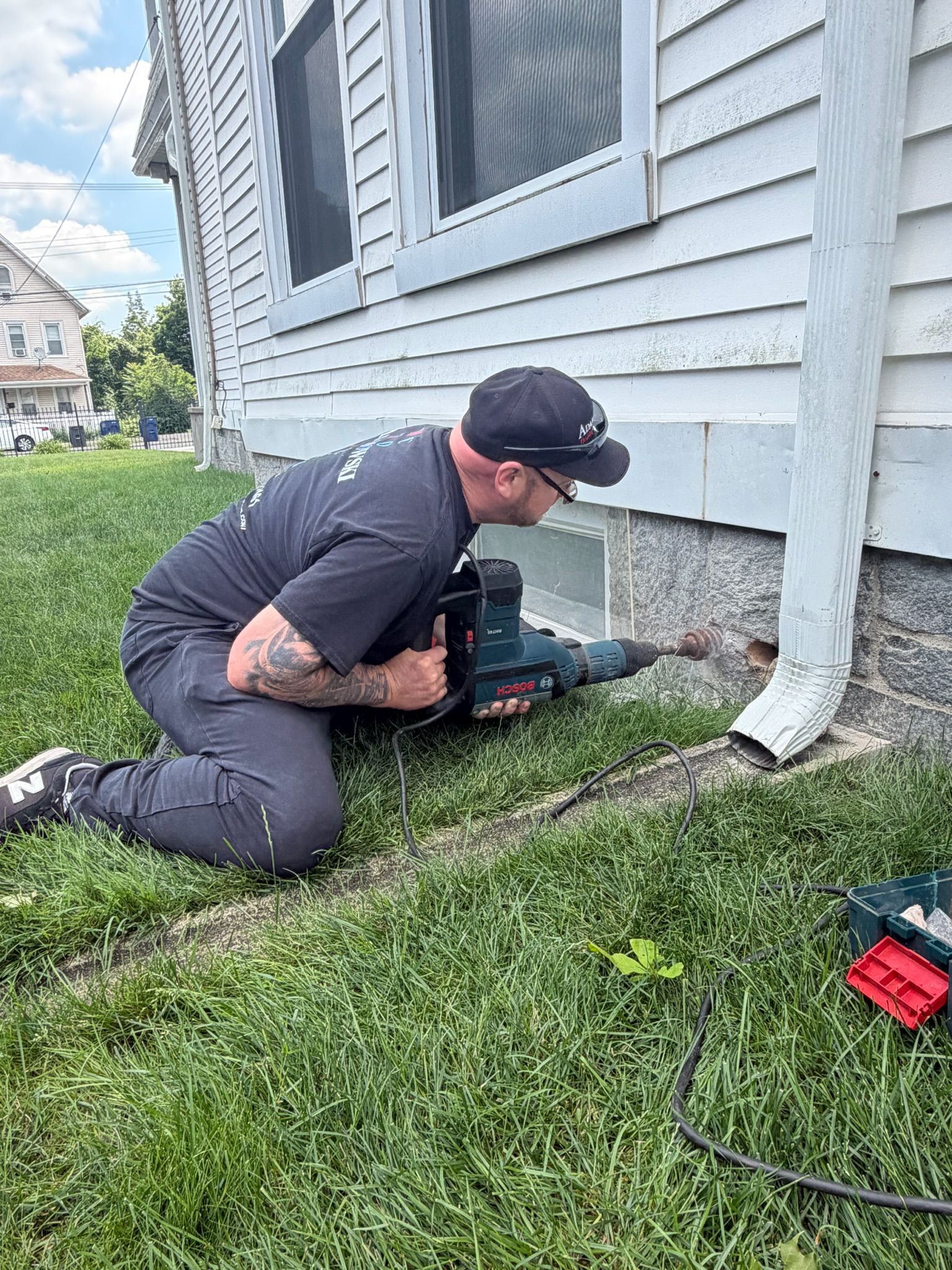 Technician drilling an exterior opening for heating oil tank fill and vent piping