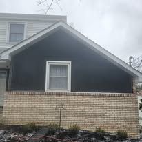 House exterior with dark siding above brick foundation, window visible.