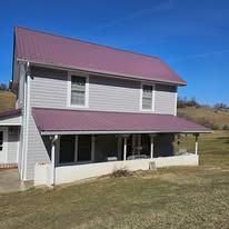 Two-story gray house with burgundy metal roof and porch against a clear blue sky.