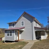 Two-story gray house with red roof, porch, and a blue sky in the background.
