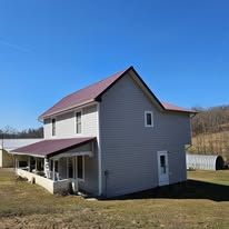 Gray two-story house with a maroon roof and porch under a clear blue sky.