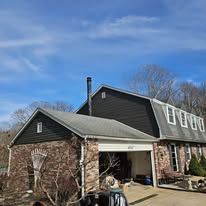 Two-story house with black siding, brick facade, garage, and a tall chimney under a blue sky.