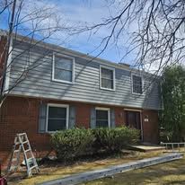 Exterior of a multi-unit building with blue siding, brick, and multiple windows. A ladder sits in front.