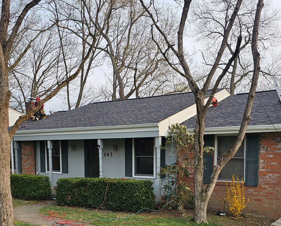 Brick house with gray roof, white porch, and two workers on the roof among leafless trees