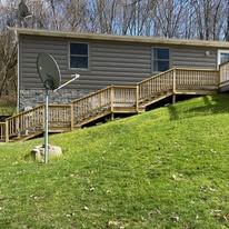 A ranch-style house with wooden siding and a deck, plus a satellite dish on a grassy lawn.