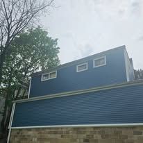 Blue sided house against a cloudy sky, showing a horizontal siding pattern and a brick foundation.