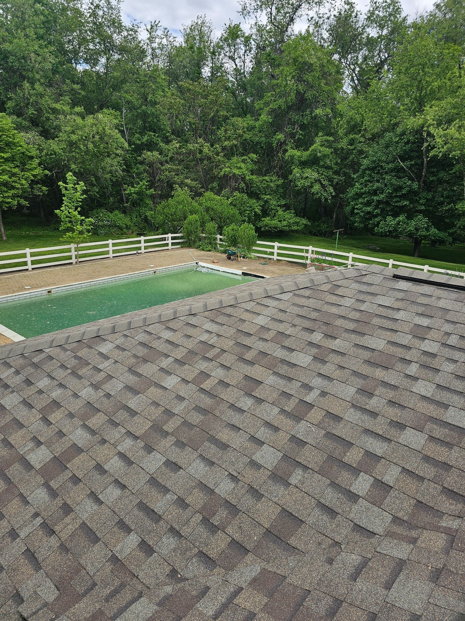 View of a mossy roof with green pool area and white fence, forest in background.