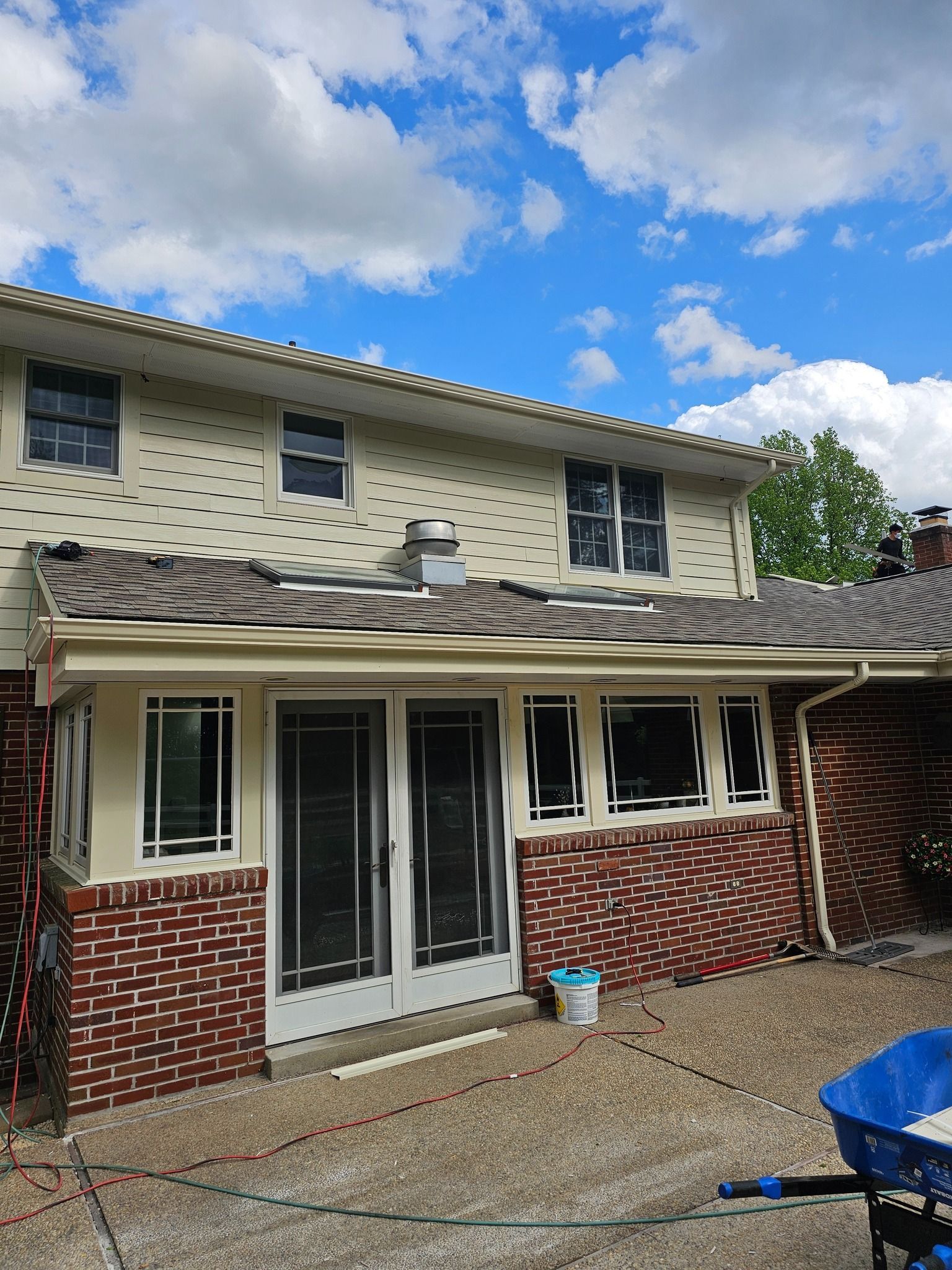 Two-story house with missing roof shingles, brick exterior, and a sunny sky.