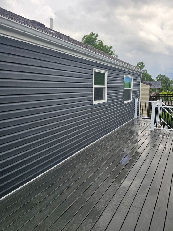 Wet gray deck beside dark gray mobile home with windows under cloudy sky