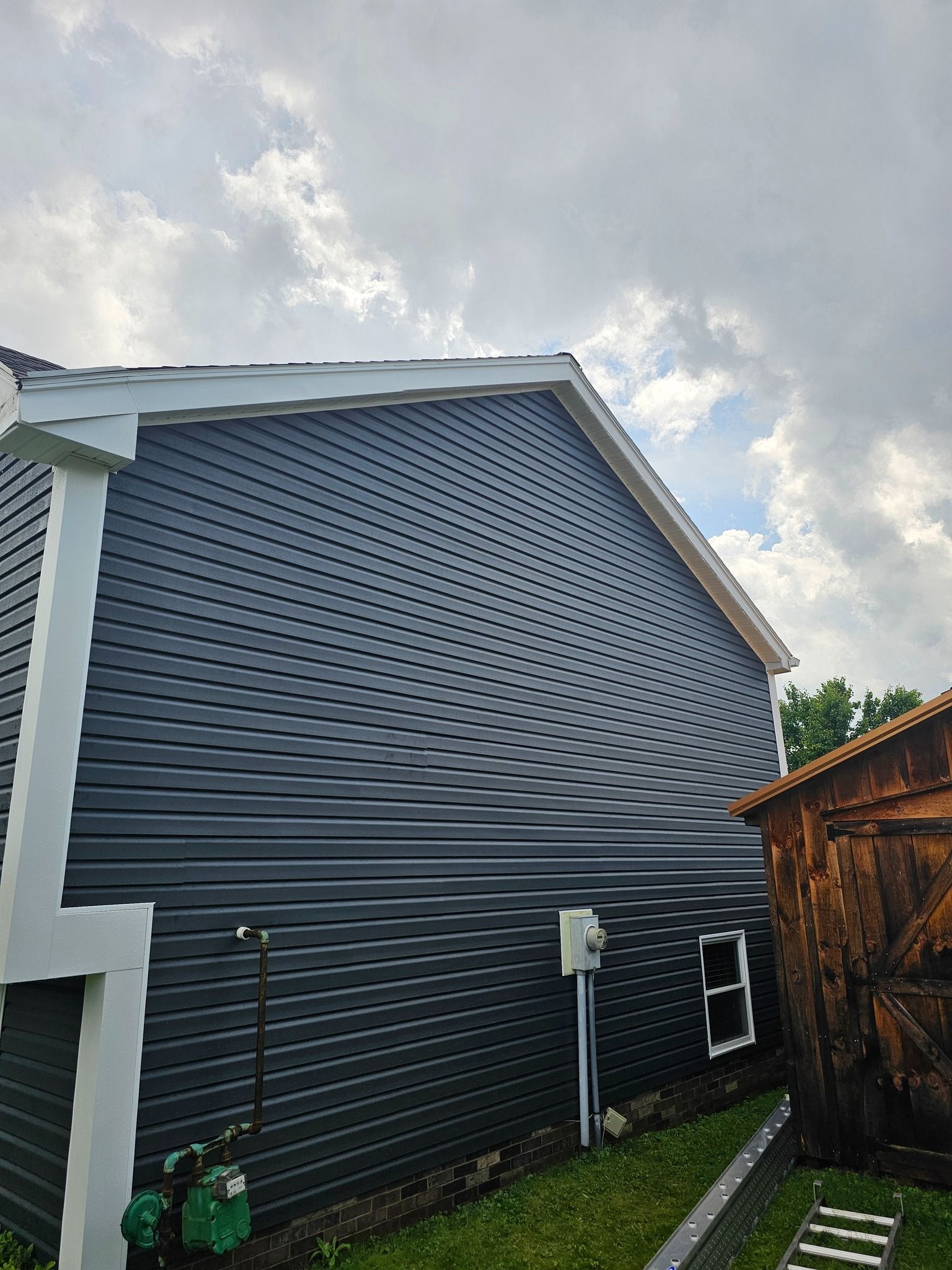 Dark blue siding on a building with white trim under a cloudy sky.