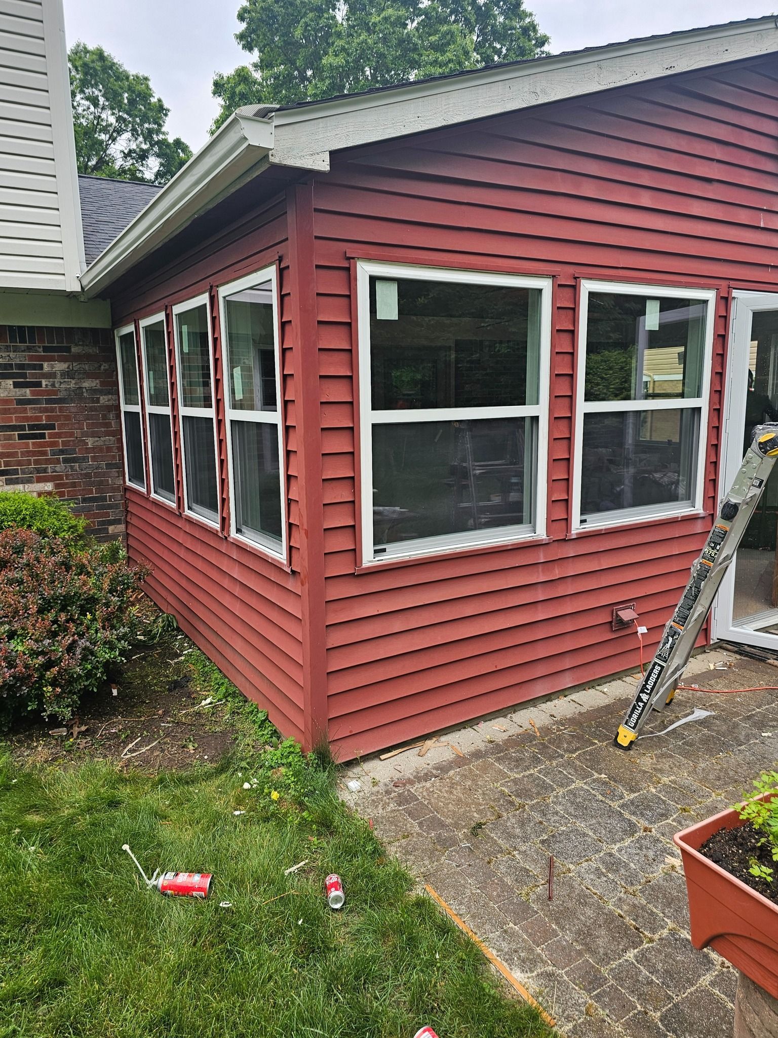 Red-sided building with several windows under construction, beside a brick house. A ladder leans against the building.