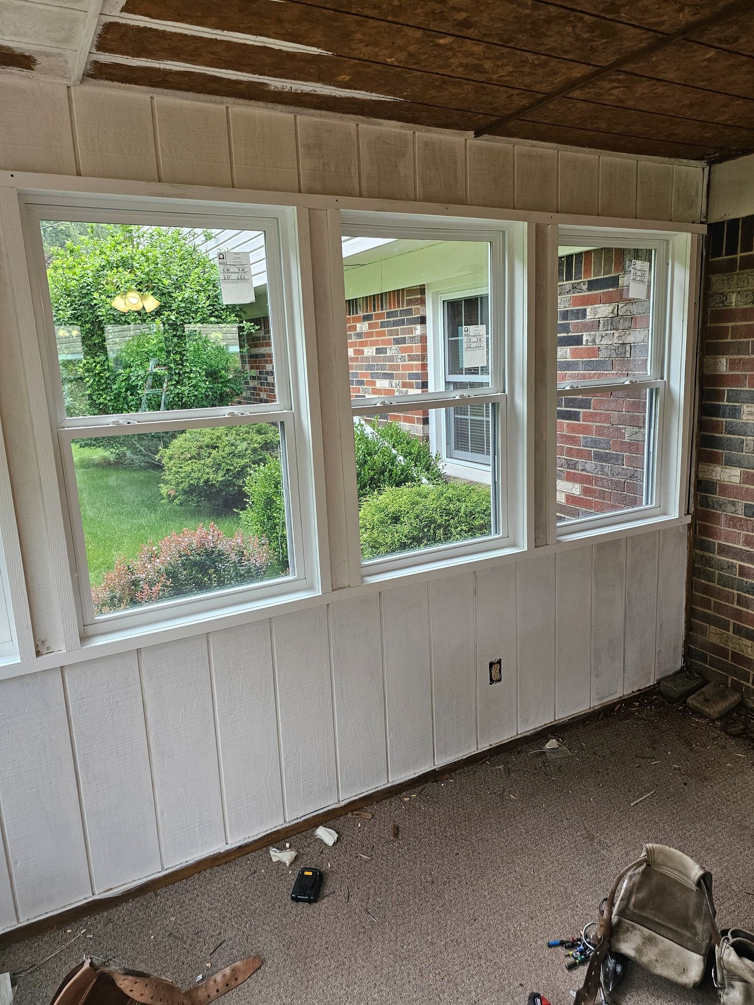 Room interior with three white framed windows, white paneling on walls, brick wall, exposed ceiling.