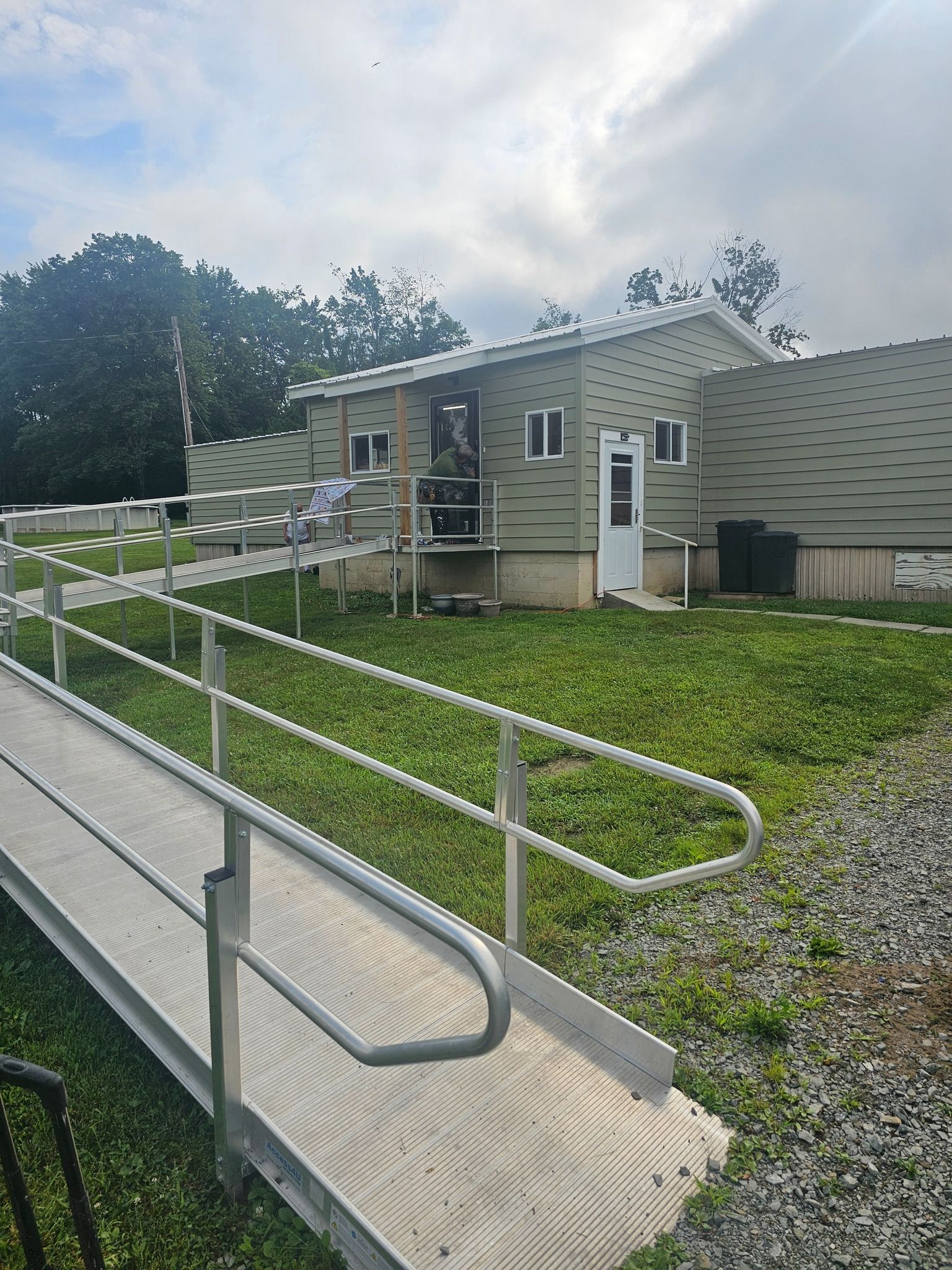 A building with a ramp for accessibility, on a grassy area, overcast sky.