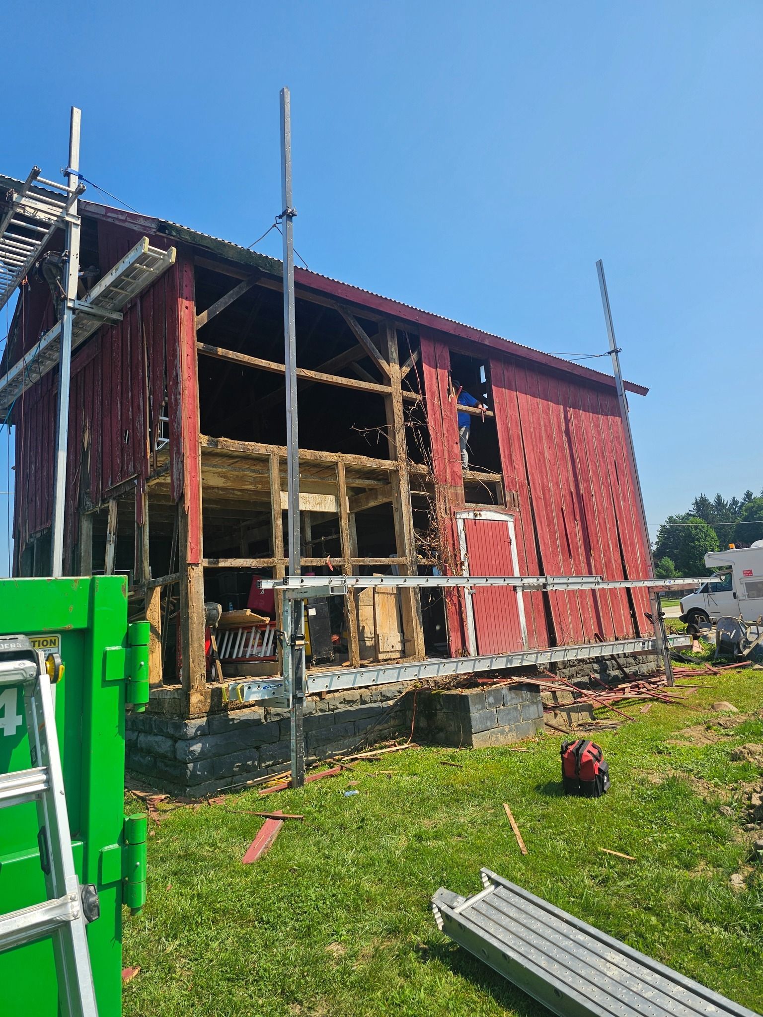 Red barn undergoing renovation, scaffolding, blue sky, green grass.