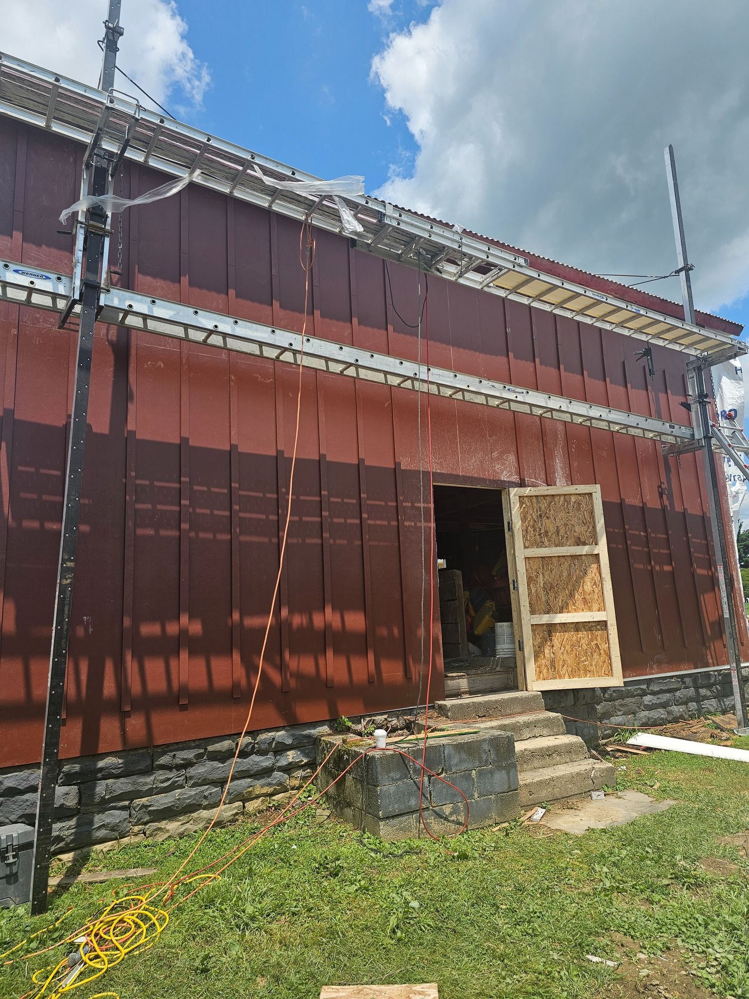 Building exterior with scaffolding, red siding, open doorway, and steps.