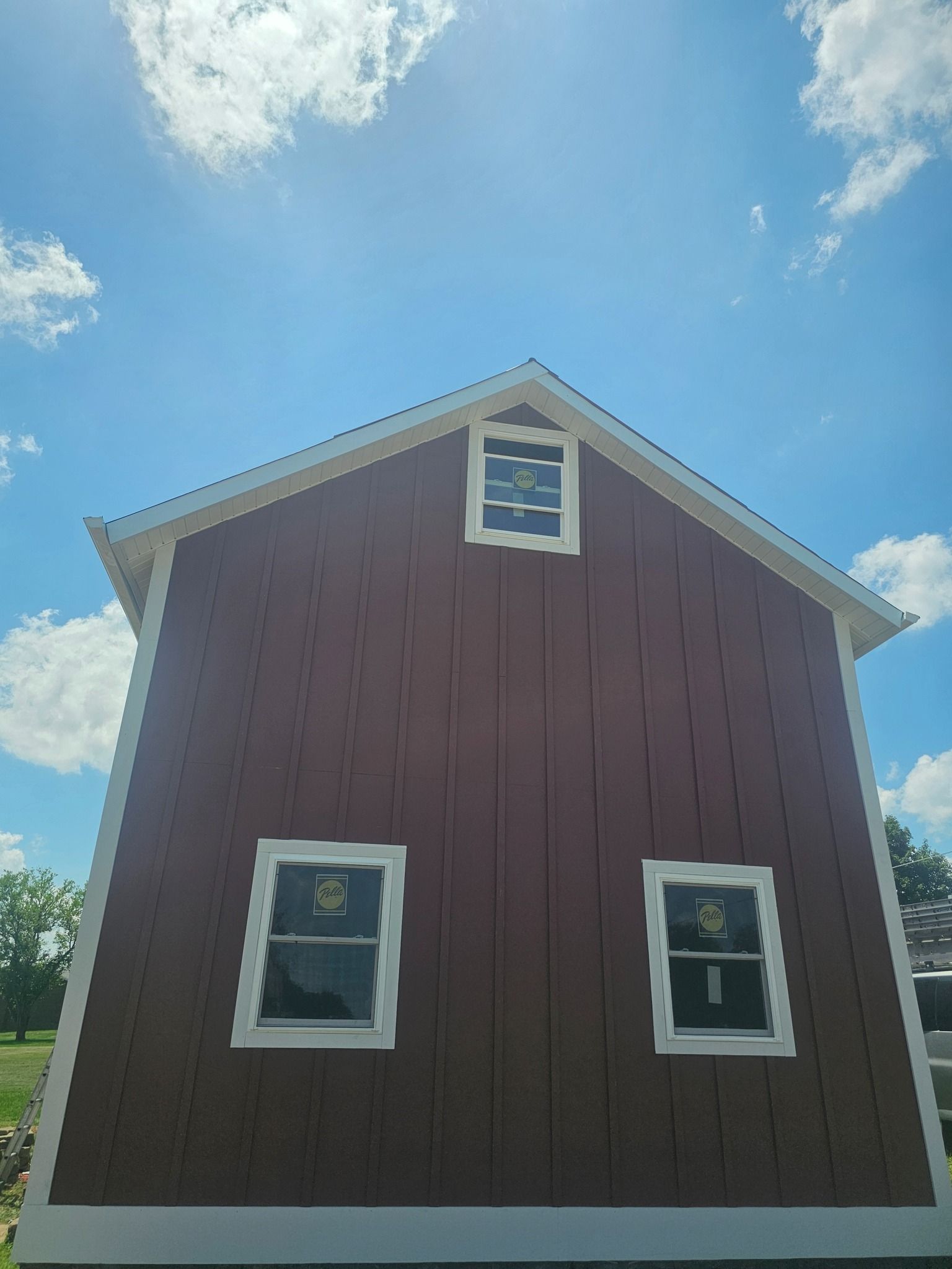 Red barn with white trim and windows against a blue sky with clouds.