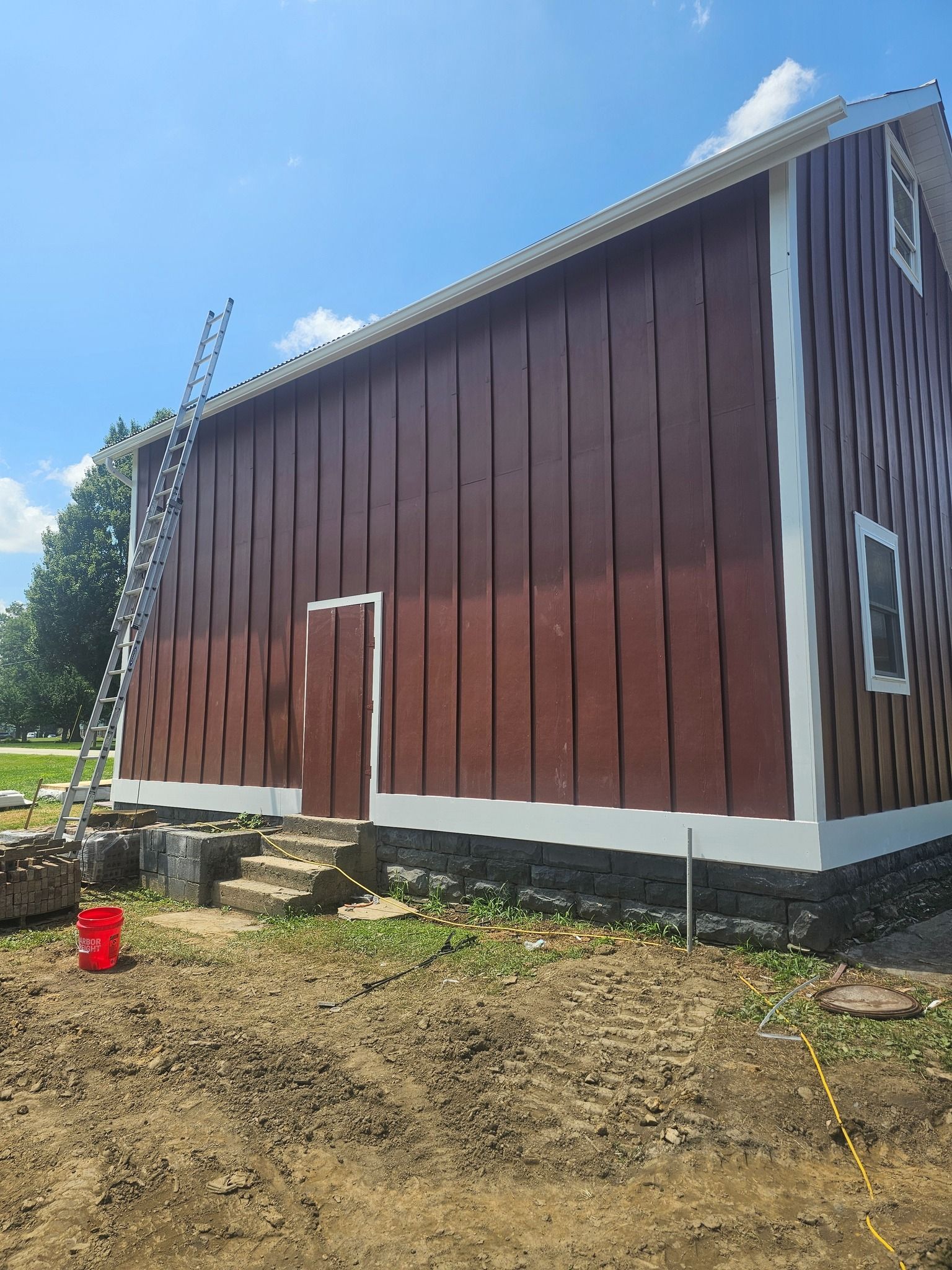 Red and white barn exterior under blue sky; a ladder leans against the wall.