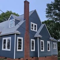 Blue house with brick chimney. Gray siding, white trim, and trees.