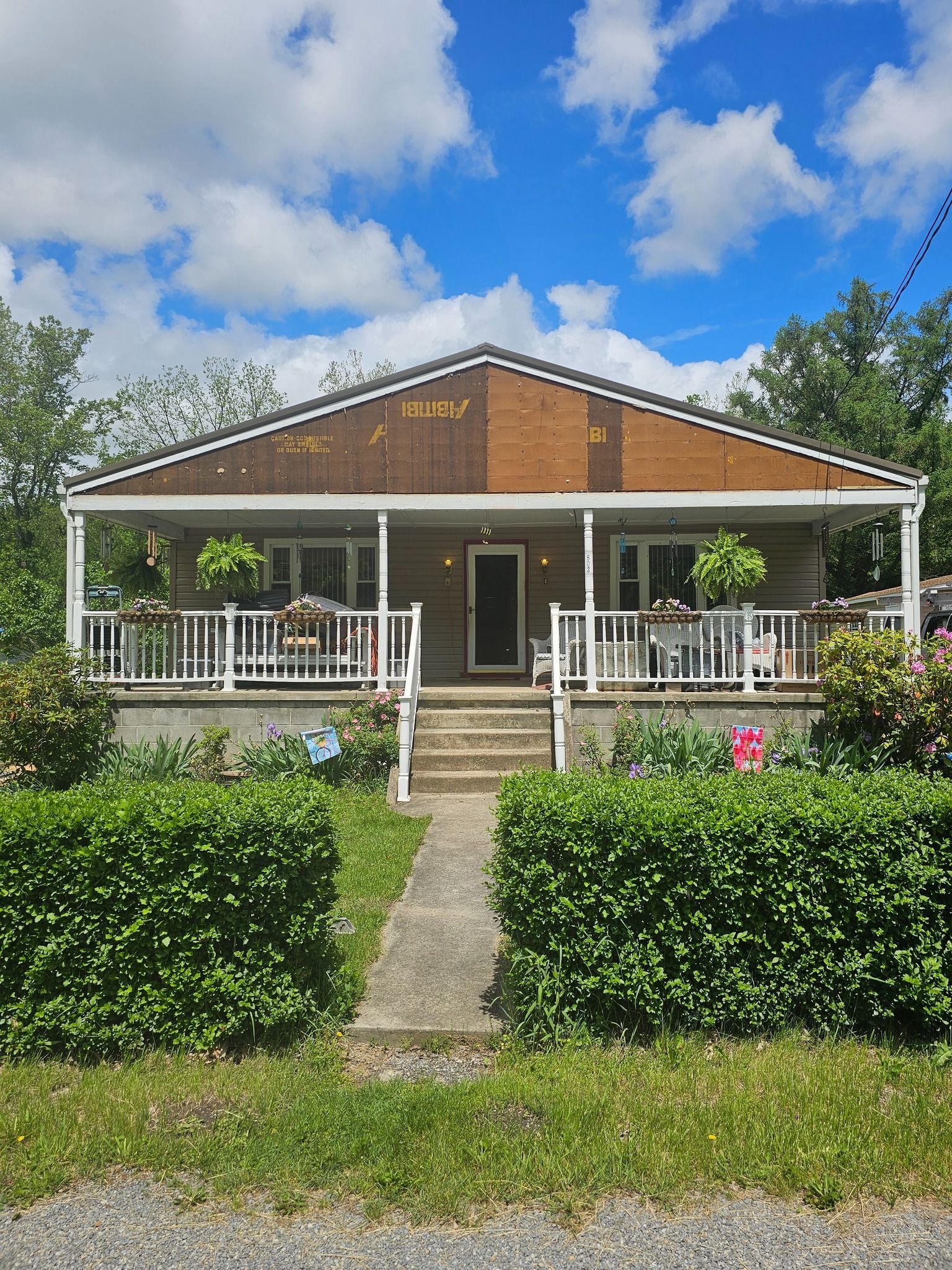 A small house with a porch, surrounded by greenery under a cloudy sky.
