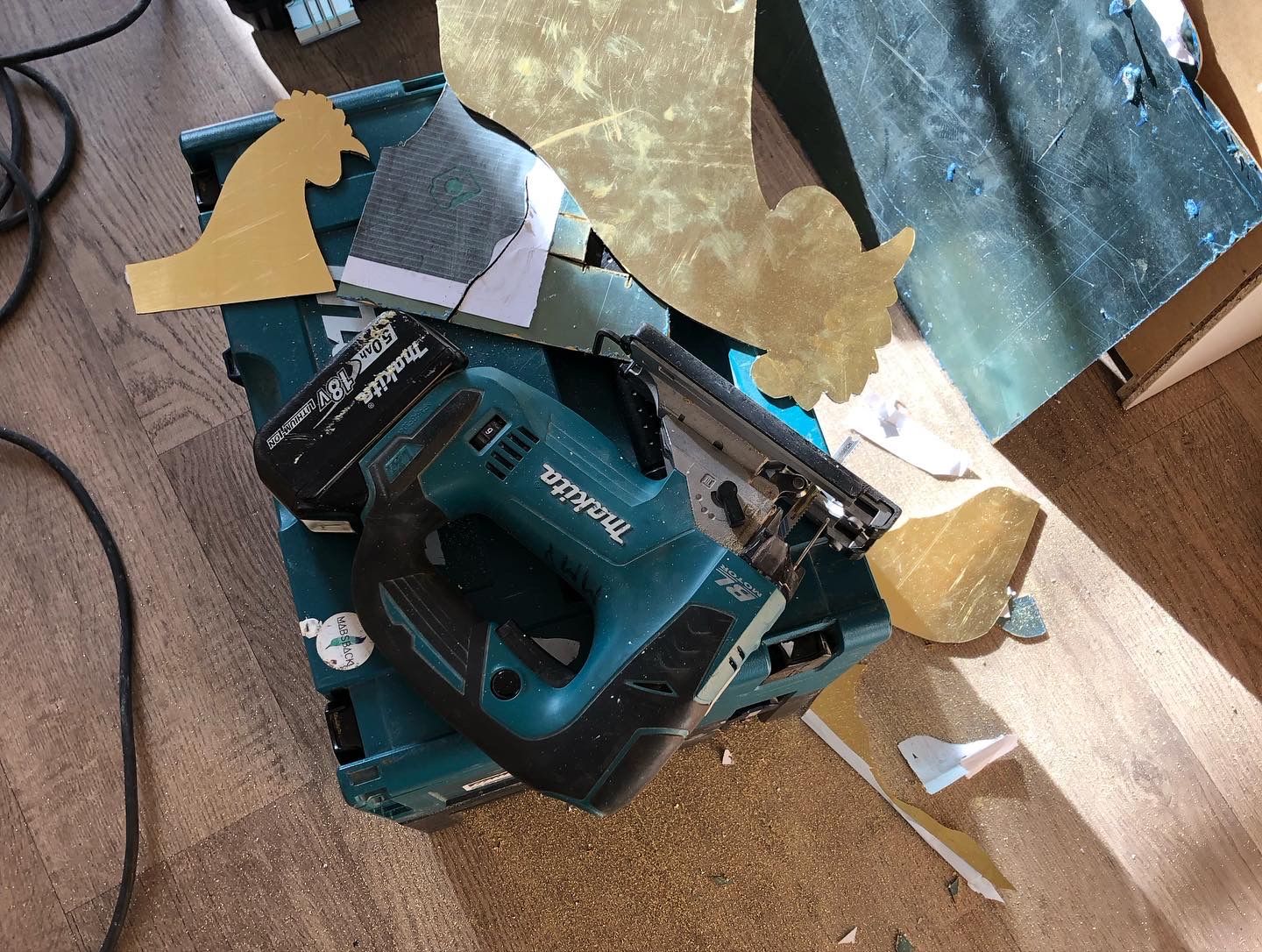 decoupeerzaag op de koffer, met uitgesneden vormen van goud en wit materiaal, op een houten vloer.