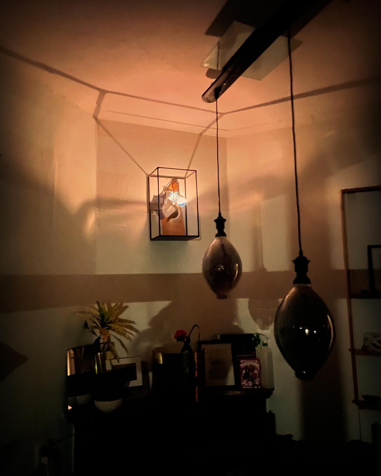 Een hoek van een kamer met hangende pendellampen en een verlichte vitrine die schaduwen werpt; warme verlichting.