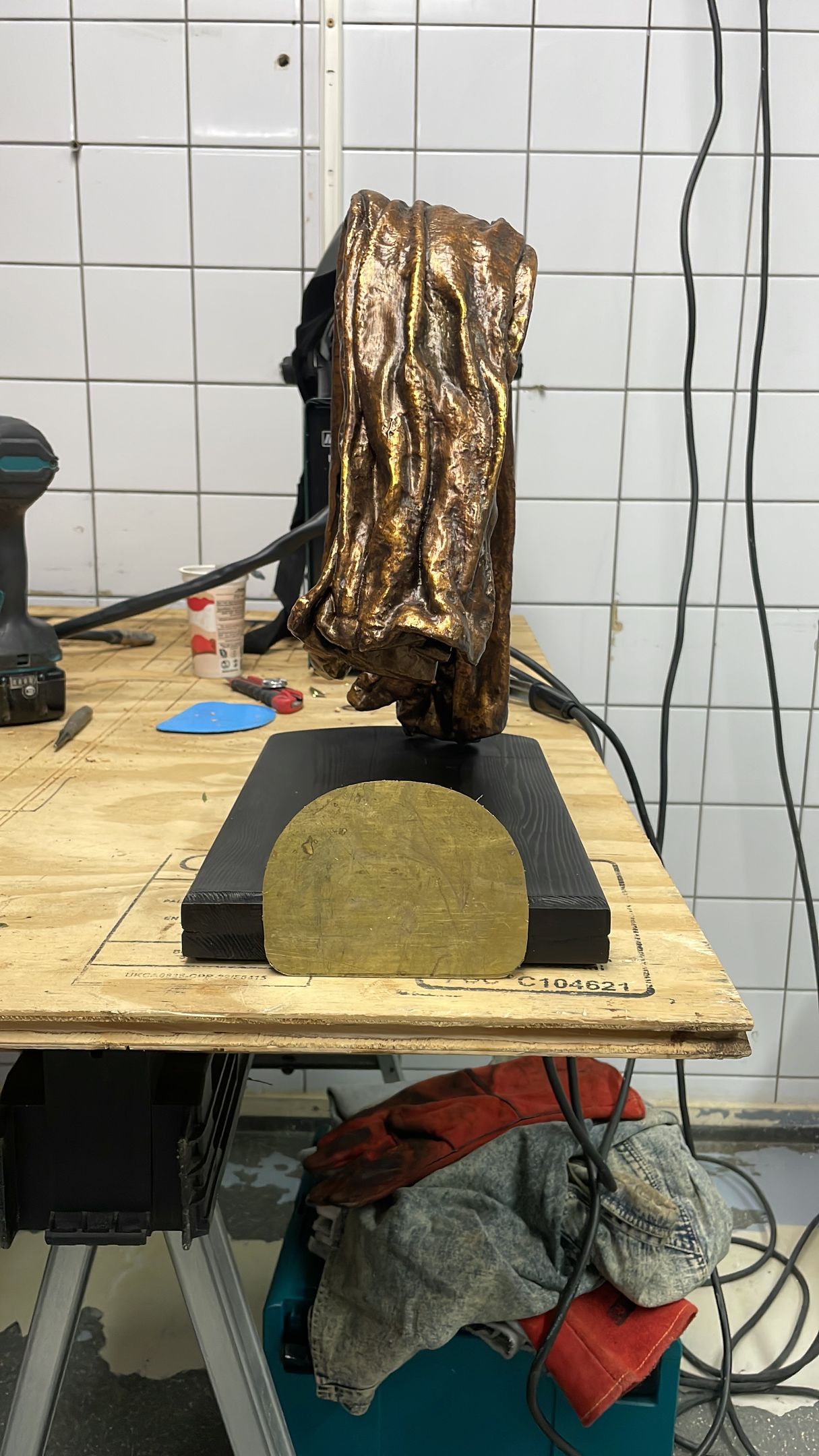 Een bronskleurige sculptuur op een zwarte sokkel, geplaatst op een houten werkbank.