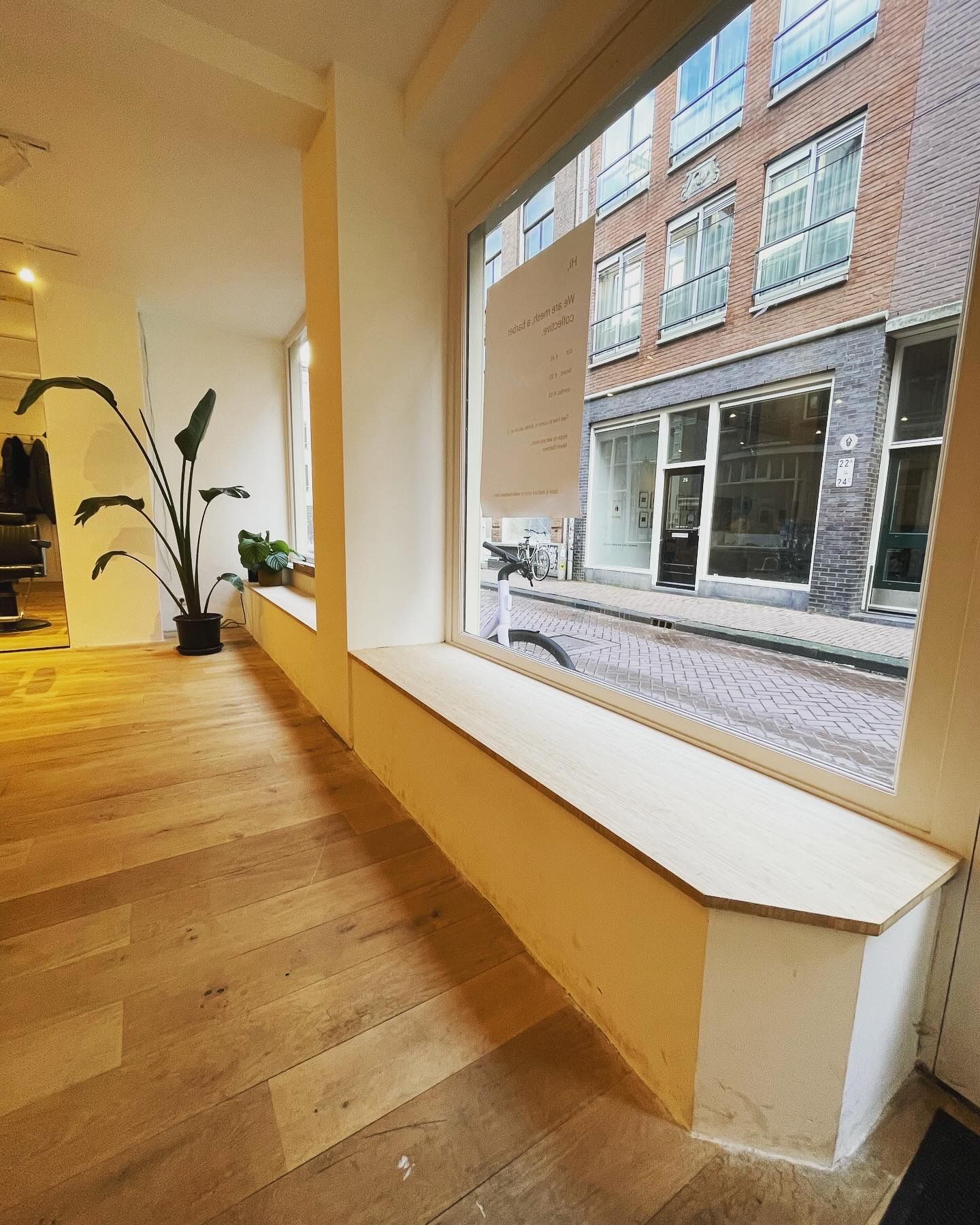 Interieur met groot raam, houten vloer en uitzicht op de straat.