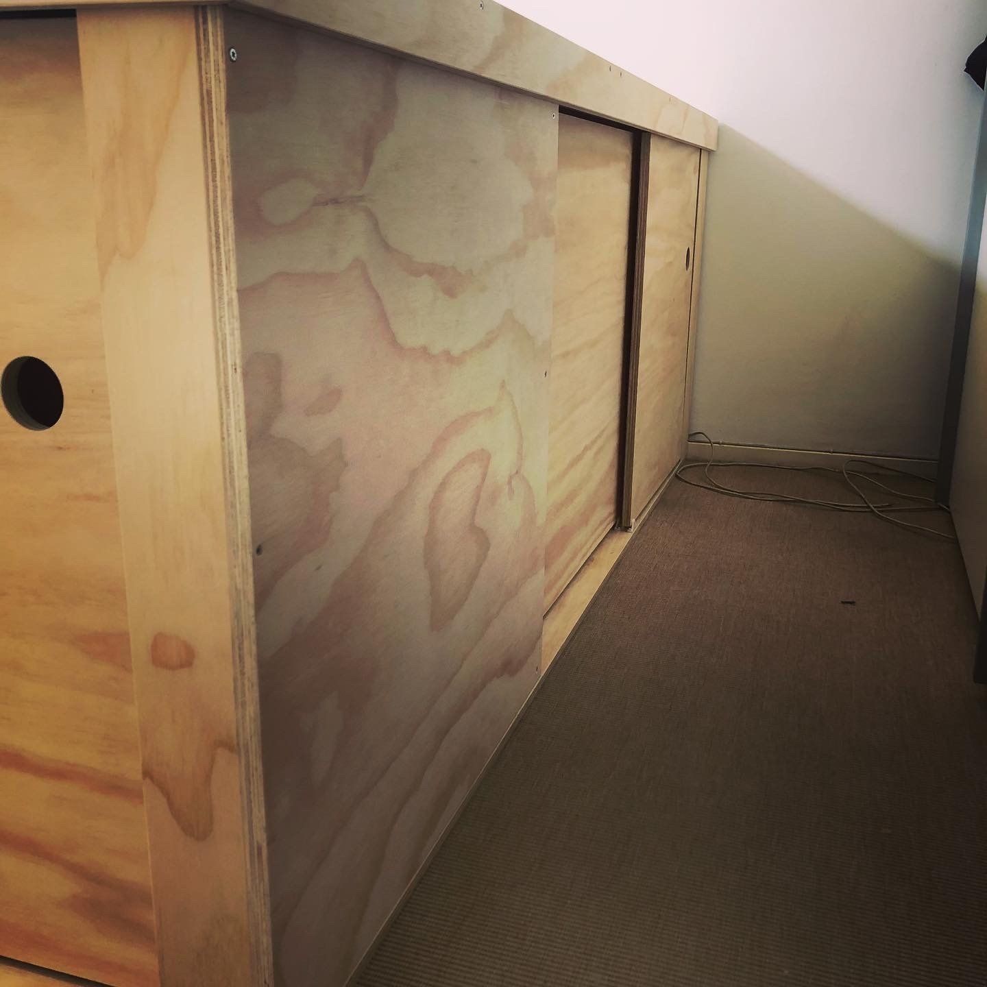 Houten opbergkast met schuifdeuren onder een schuin plafond. In het zijpaneel zit een donker gat.