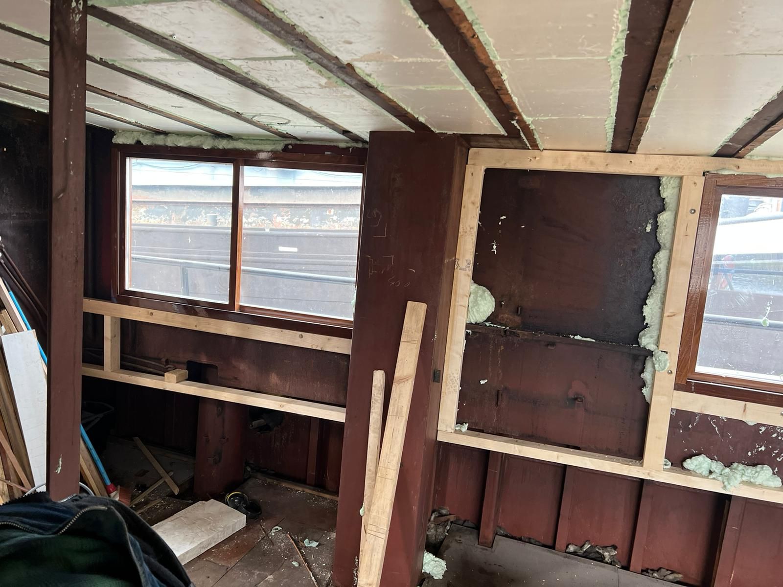 Interieur van een kamer in aanbouw met houten lambrisering, ramen en zichtbare plafondbalken.