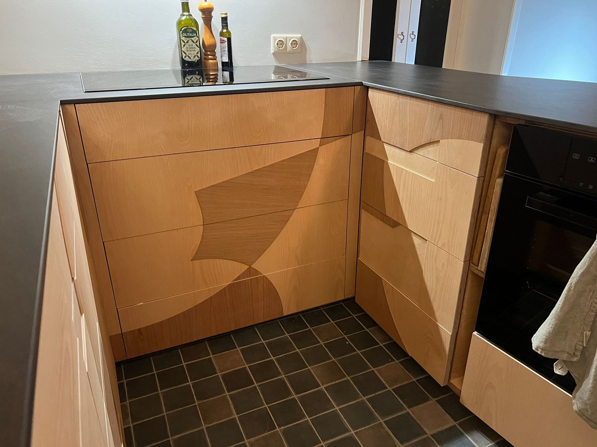 Keukenkasten met houtnerfdesign, donkere werkbladen en een zwarte tegelvloer.